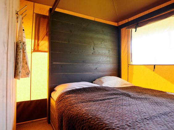 De knusse ouderslaapkamer in een safaritent op Vakantiepark Sallandshoeve, met een comfortabel opgemaakt tweepersoonsbed.