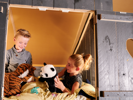 Een broer en zus spelen met hun knuffels in de knusse, houten bedstee van hun safaritent op Vakantiepark Sallandshoeve.