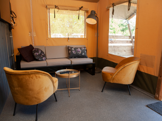 De stijlvolle en comfortabele zithoek in een safaritent op Sallandshoeve, met een bank en zachte, gele fluwelen stoelen.