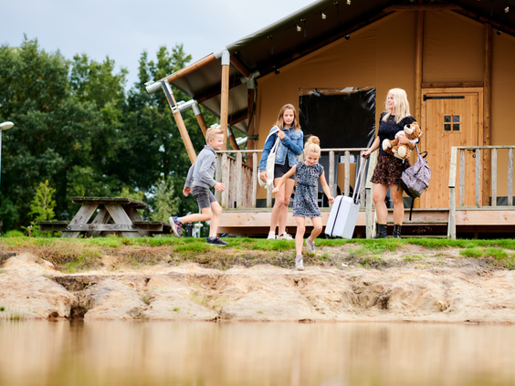 Een gezin loopt langs de oever van de speelvijver naar hun safaritent op vakantiepark Sallandshoeve in Overijssel.