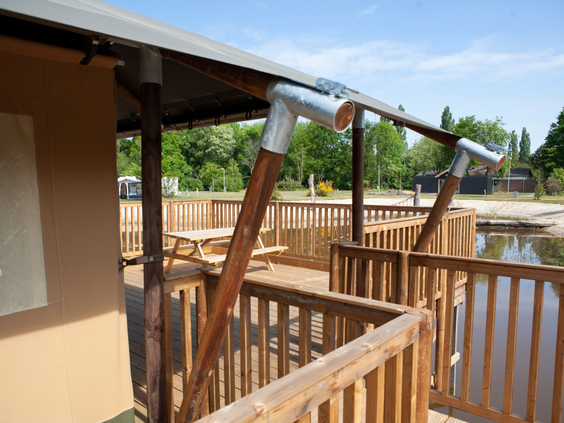 De ruime houten veranda van een safaritent op Vakantiepark Sallandshoeve, direct gelegen aan de speelvijver.