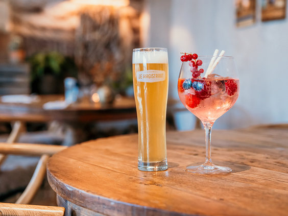 Een glas bier en een kleurrijke cocktail met rood fruit staan op een houten tafel in het restaurant van De Zeeuwse Kust.