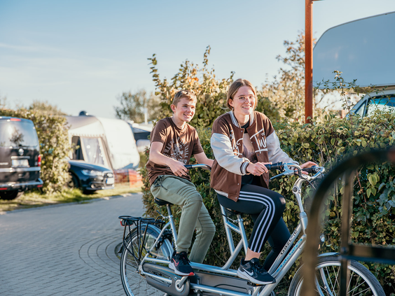 Twee kinderen rijden samen op een tandemfiets over het vakantiepark bij de camping van Strandpark De Zeeuwse Kust.