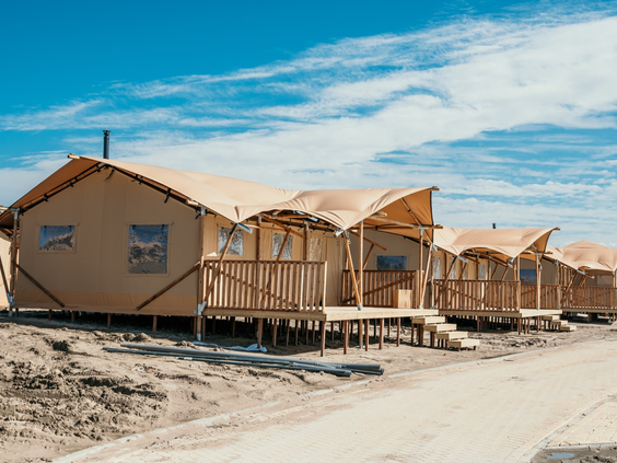 Een rij met luxe safaritenten voor glamping op het zandstrand van Strandpark De Zeeuwse Kust onder een strakblauwe lucht.