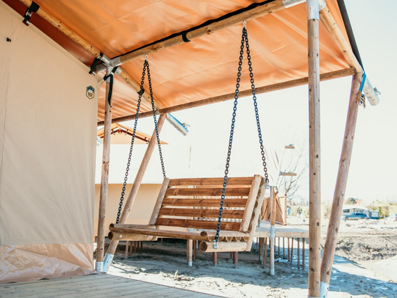Een houten schommelbank op de veranda van een luxe safaritent op Strandpark De Zeeuwse Kust.