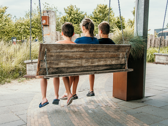 Kinderen maken plezier op een houten schommelbank in de speeltuin van Strandpark De Zeeuwse Kust, een leuke activiteit voor het hele gezin.