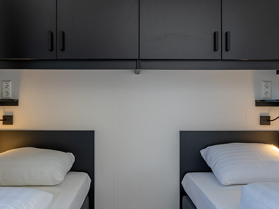 Praktisch ingerichte slaapkamer met twee bedden en handige opbergkastjes erboven in een accommodatie op Strandpark De Zeeuwse Kust.
