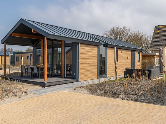 Buitenaanzicht van een modern en ruim opgezet chalet met een grote veranda, gelegen in het duinlandschap van Strandpark De Zeeuwse Kust.