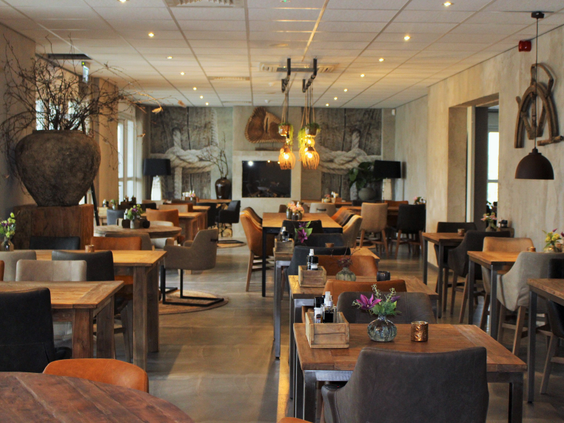 Het sfeervolle en ruime interieur van het familierestaurant bij Strandpark De Zeeuwse Kust met houten tafels en stoelen.