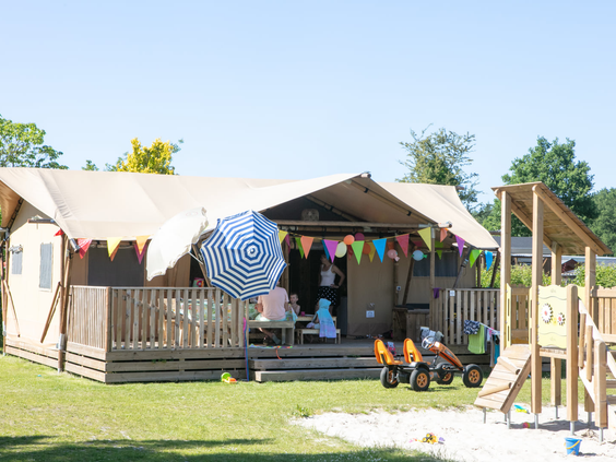 Een luxe safaritent op Camping 't Veld met een eigen omheinde tuin en een houten speeltoestel met glijbaan voor de kinderen.