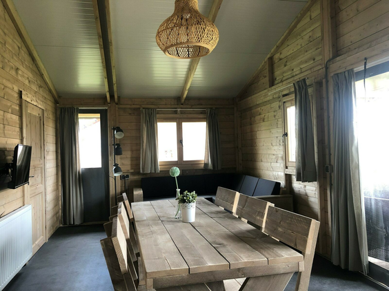 De ruime en sfeervolle houten inrichting van een lodge op Camping 't Veld, met een grote eettafel en zithoek.