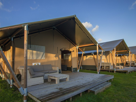 De ruime houten veranda van een luxe lodge op Camping 't Veld, met een comfortabele loungeset in de avondzon.