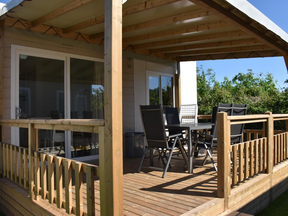 De ruime, overdekte houten veranda van een lodge op Camping 't Veld, met een comfortabele tuinset.