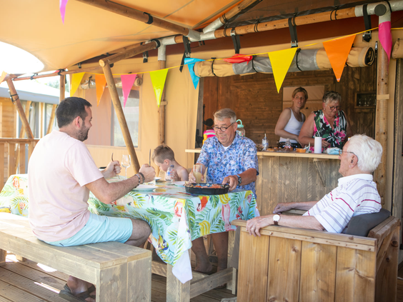 Een gezelschap geniet van een drankje en een hapje op het gezellige, overdekte terras bij de horeca van Camping 't Veld.