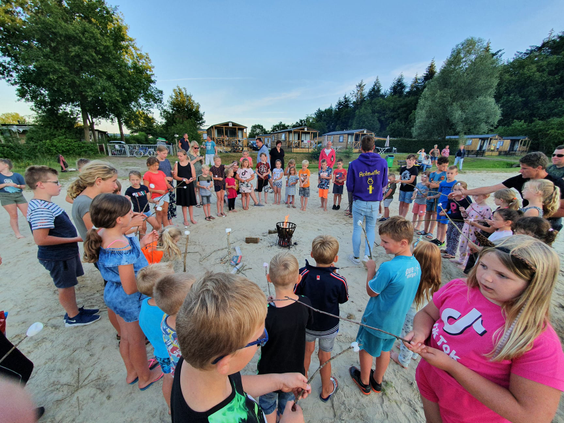 Een grote groep kinderen verzamelt zich op het strand voor een leuke activiteit met het animatieteam van Camping 't Veld.