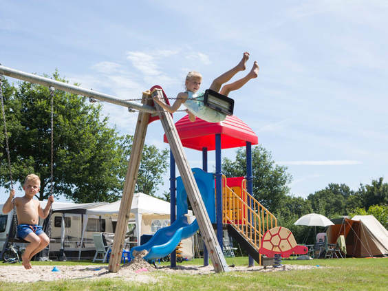 Kinderen hebben plezier in de speeltuin, waar een jongen hoog op de schommel zwiert bij een klimtoestel met glijbaan.