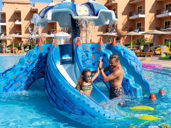 Een vader en dochter hebben plezier op een kleine blauwe kinderglijbaan in het zwembad van Three Corners Sunny Beach Resort.