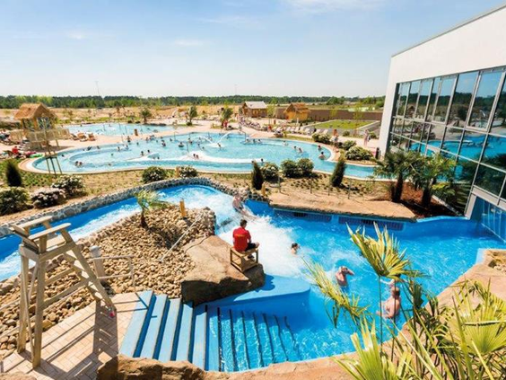 Bezoekers genieten van de zon en het water in het buitenzwembad AMAZONIA bij Tropical Islands, met de wildwaterbaan op de voorgrond.