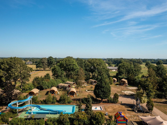 Een luchtfoto van Vakantiecentrum 't Schuttenbelt in Twente, met het grote buitenzwembad met waterglijbaan en de lodges in een groene omgeving.