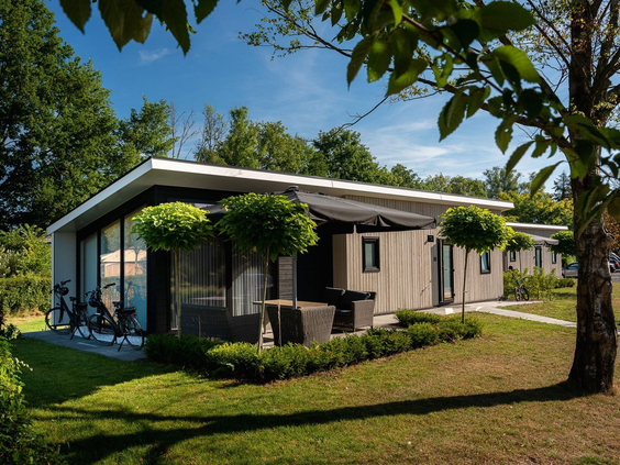 De buitenkant van een moderne en luxe Regge Cottage op Vakantiecentrum 't Schuttenbelt, gelegen in het groen met een ruim terras.