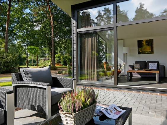 Het zonnige terras van een Regge Cottage met een comfortabele loungeset, met uitzicht op de woonkamer door de grote glazen pui.