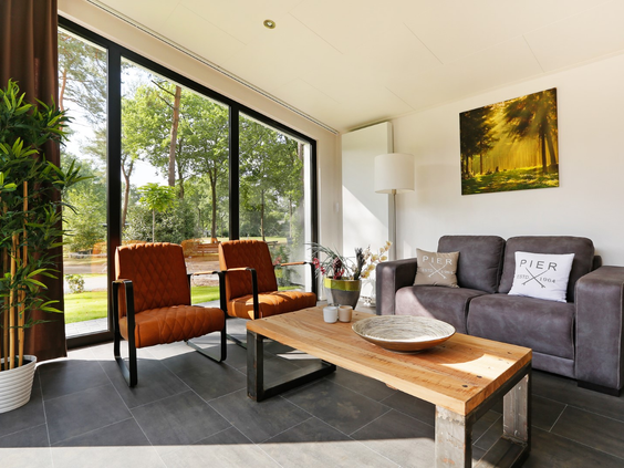 De lichte en moderne woonkamer van een Regge Cottage op Vakantiecentrum 't Schuttenbelt, met grote ramen die uitkijken op de groene natuur.