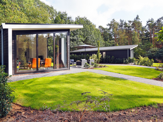 Twee moderne Regge Cottages op Vakantiecentrum 't Schuttenbelt, omgeven door een ruim en groen grasveld, ideaal voor spelende kinderen.