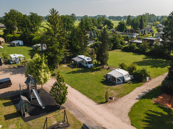Ruime kampeerplaatsen met caravans op Vakantiecentrum 't Schuttenbelt, met op de voorgrond een leuke speeltuin voor de kinderen.