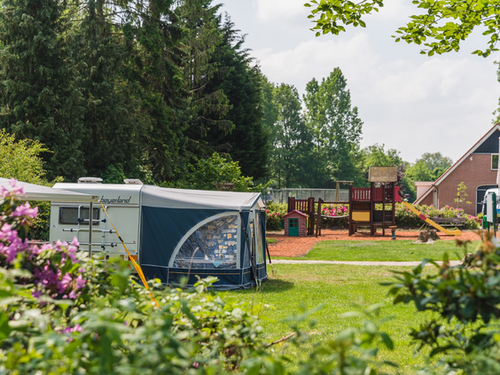 Een ruime kampeerplaats op Vakantiecentrum 't Schuttenbelt met een caravan, direct grenzend aan de speeltuin voor de kinderen.