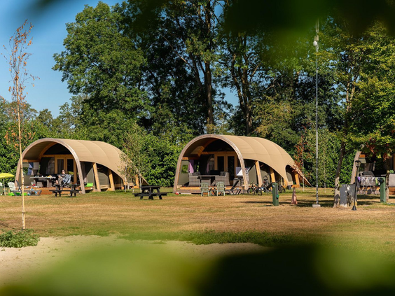 Twee luxe en uniek vormgegeven lodges op een groot grasveld, omringd door bomen op Vakantiecentrum 't Schuttenbelt.