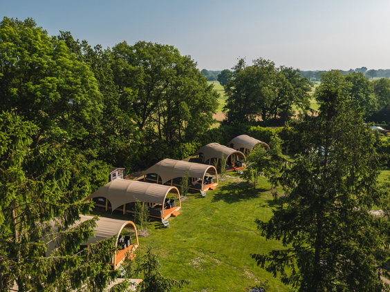 Een luchtfoto die een rij luxe lodges laat zien, prachtig verscholen in het groene en bosrijke landschap van het vakantiepark in Overijssel.
