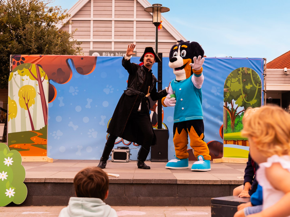 Kinderen kijken naar een animatieshow op het buitenpodium van Vakantiepark Aquadelta, met de mascotte en een entertainer.