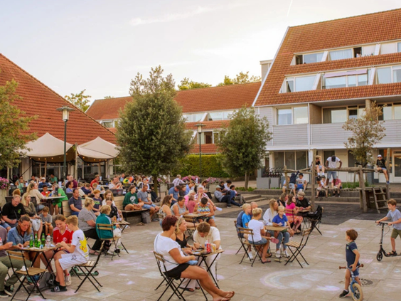 Gezellige drukte op het centrale plein van Vakantiepark Aquadelta, met volle terrassen en spelende kinderen.