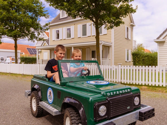 Twee jongetjes rijden lachend in een groene elektrische kinderauto in de vorm van een jeep over Vakantiepark Aquadelta.
