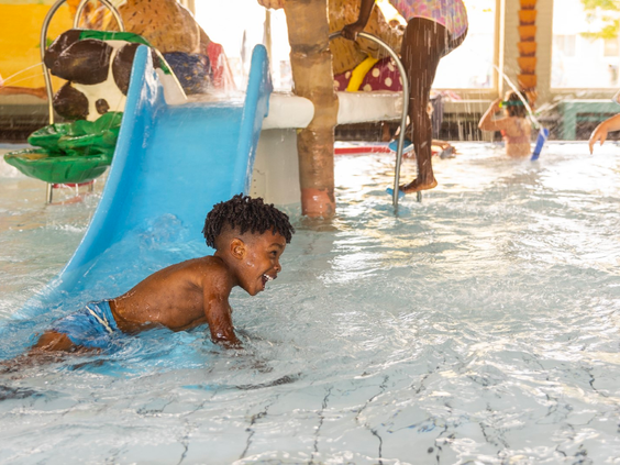 Een klein jongetje heeft waterpret bij de peuterglijbaan in het kinderbad van het overdekte zwembad op Vakantiepark Aquadelta.