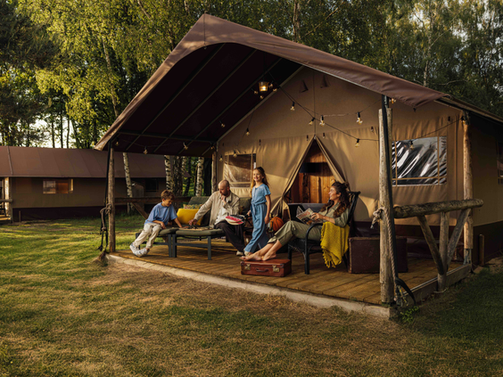 Gezin van vier ontspant samen op de veranda van een ruime safaritent in het bos van Lake Resort Beekse Bergen