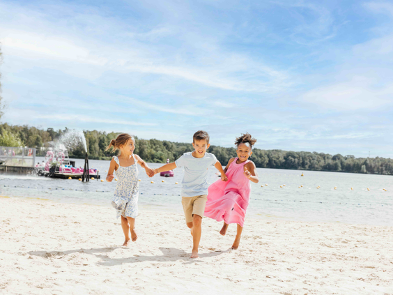 Drie lachende kinderen rennen hand in hand over het zandstrand van Lake Resort Beekse Bergen