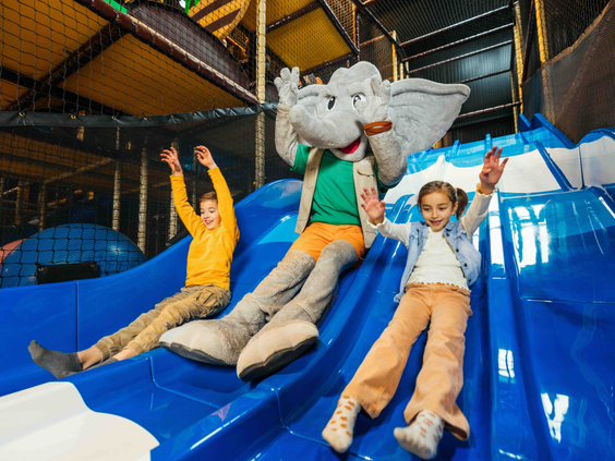 Twee kinderen glijden lachend van een blauwe glijbaan met mascotte Djambo in Speelland Beekse Bergen