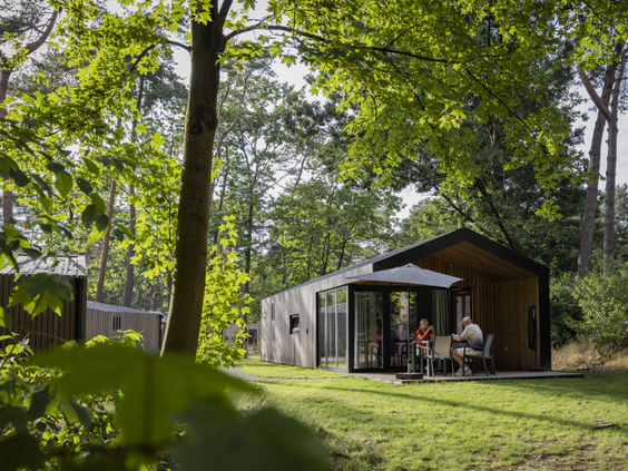 Een gezin geniet op het overdekte terras van hun moderne vakantiehuis in het bos op Vakantiepark Bospark 't Wolfsven.
