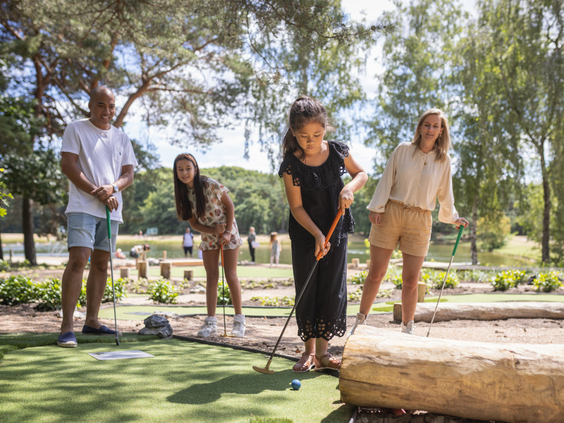 Een gezin speelt een potje avontuurlijk midgetgolf op de groene buitenbaan van Vakantiepark Bospark 't Wolfsven.