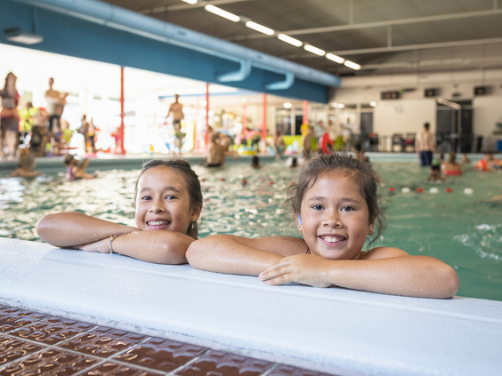 Twee lachende meisjes hebben waterpret en hangen aan de rand van het binnenzwembad op Vakantiepark Bospark 't Wolfsven.
