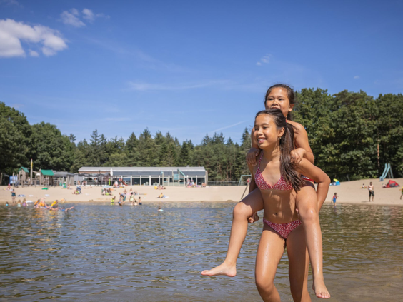 Twee lachende meisjes in badkleding spelen in het ondiepe water van het recreatiemeer bij het zandstrand van Bospark 't Wolfsven.