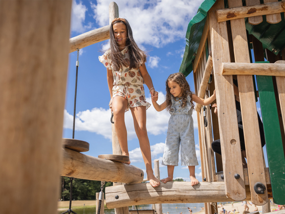 Twee meisjes klimmen en spelen samen op een houten klimtoestel in de natuurspeeltuin van Vakantiepark Bospark 't Wolfsven.
