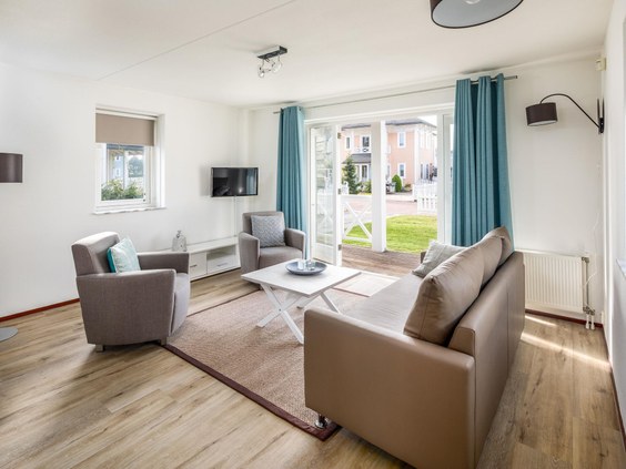 De gezellige woonkamer van een vakantiehuis op Vakantiepark Cape Helius met een comfortabele zithoek en openslaande deuren.