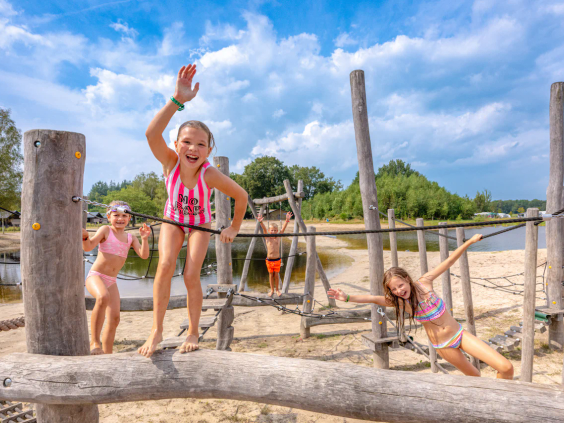 Kinderen spelen op boomstammen en in het zand in de avontuurlijke natuurspeeltuin