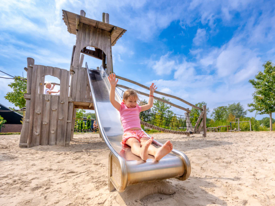 Kind op een houten glijbaan in een grote zandbak op het vakantiepark