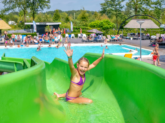 Een meisje glijdt vrolijk van de bochtige groene waterglijbaan in het waterpark