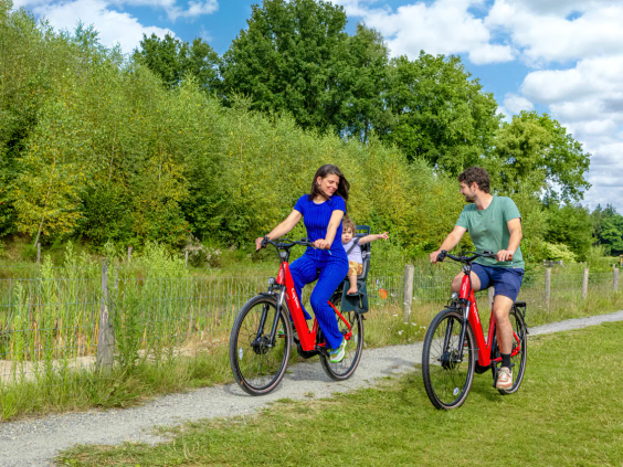Een gezin fietst vrolijk door de groene en bosrijke omgeving van de camping