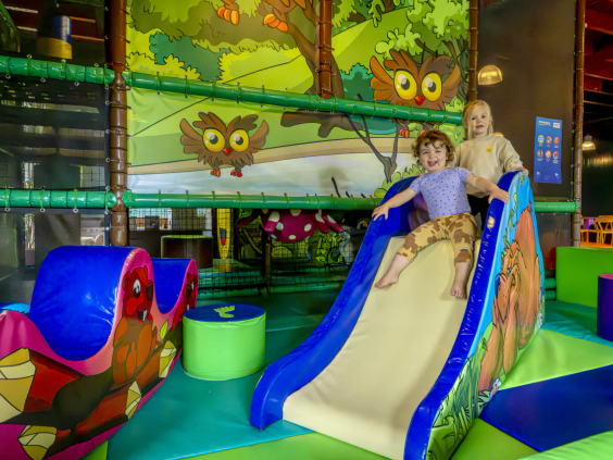 Kinderen in de overdekte binnenspeeltuin met een veilige glijbaan en klimnetten