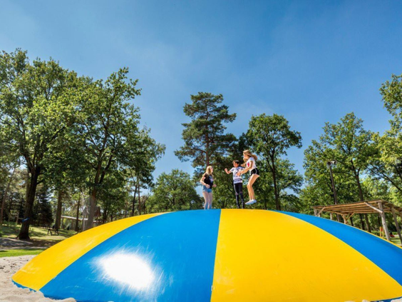 Kinderen springen hoog in de lucht op de grote, blauw-gele airtrampoline bij Vakantiepark De Bergen.